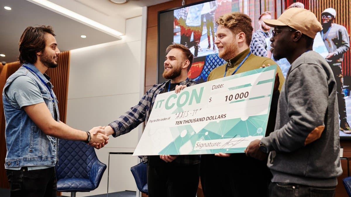 A group of men celebrating a win and receiving a large cheque at an IT conference.