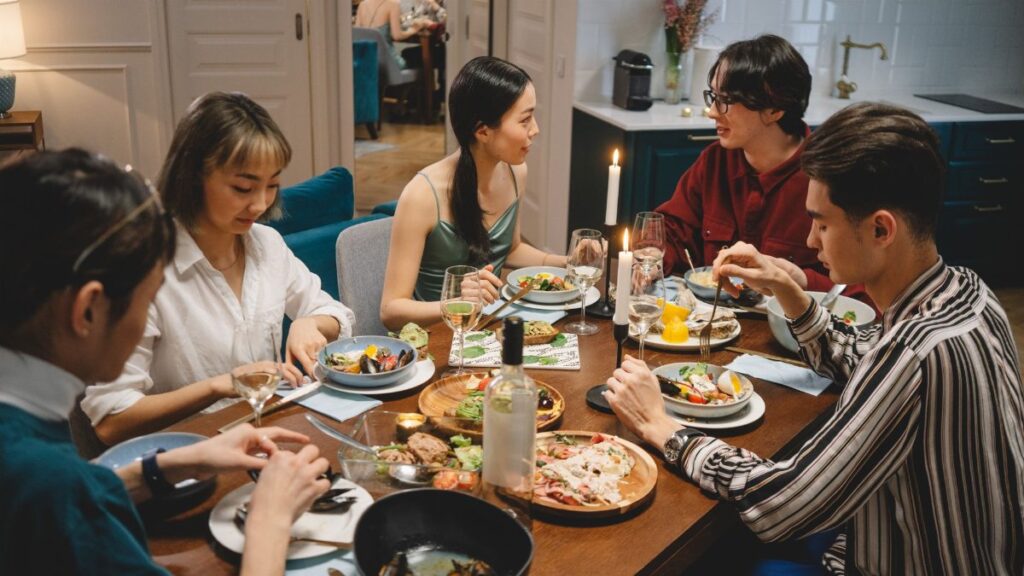 A diverse group of friends sharing dinner at a cozy dining table with wine and lighted candles.