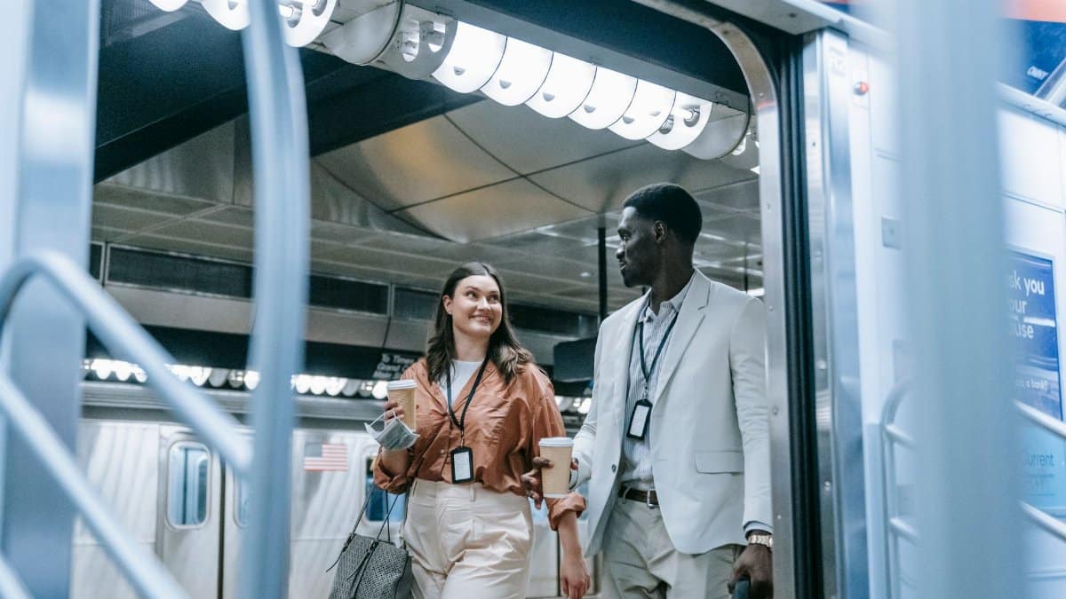 Two colleagues carrying cups exit a public subway train platform.