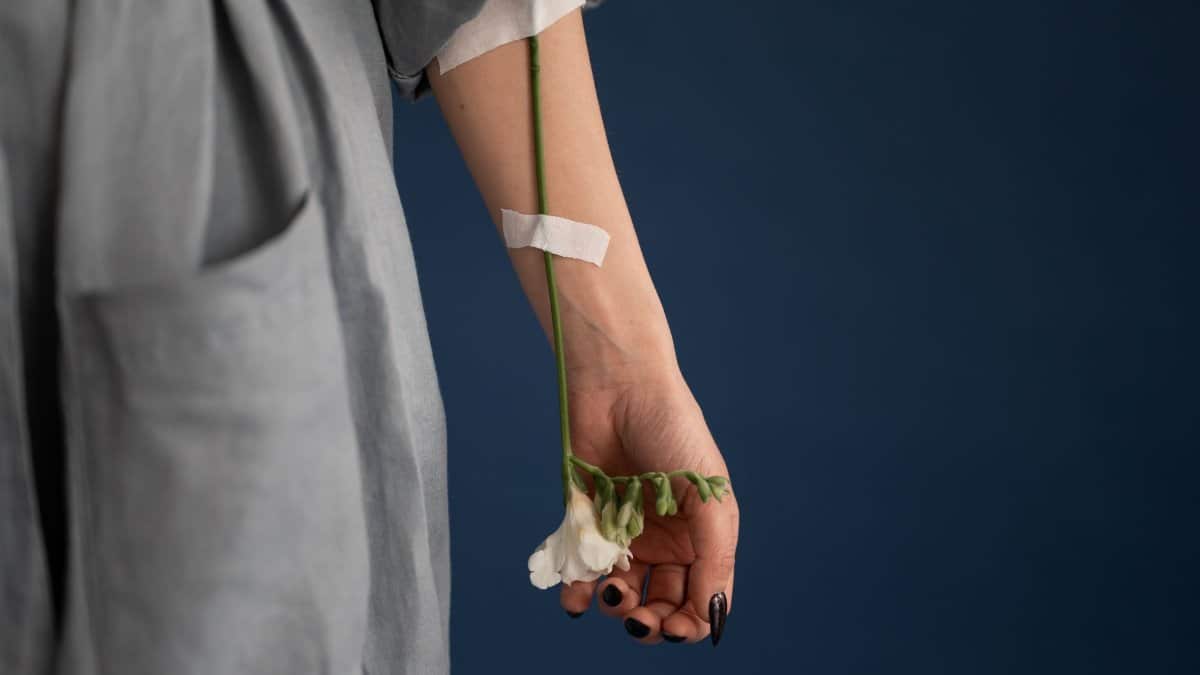 Crop anonymous female in gray robe with delicate white flower attached to arm with plaster in studio