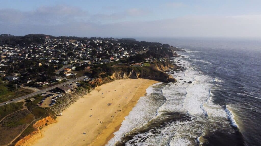 Stunning aerial shot of Half Moon Bay, CA coastline with sandy beach and waves.