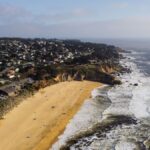 Stunning aerial shot of Half Moon Bay, CA coastline with sandy beach and waves.