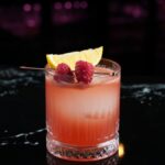 Vibrant raspberry cocktail garnished with lemon slice on a bar counter, perfect for a refreshing drink.