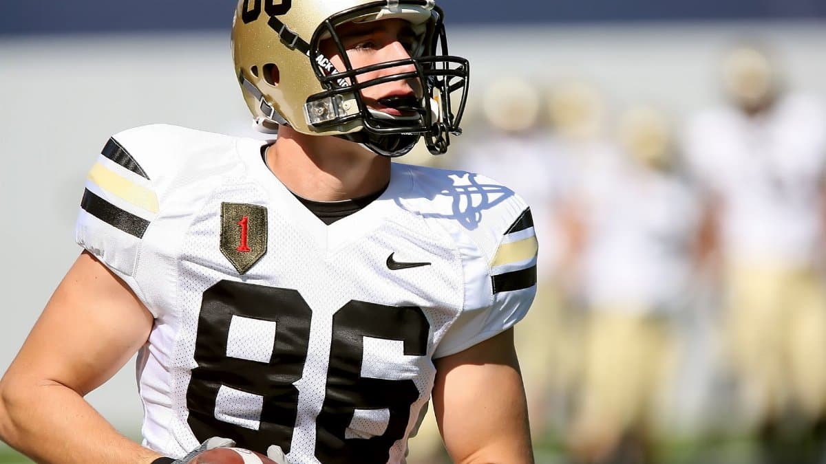 Focused college football player in uniform holding a football during a game.