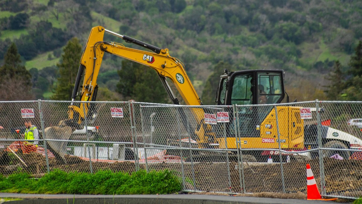 Excavator working at a construction site with safety fences and workers, depicting industry work environment.