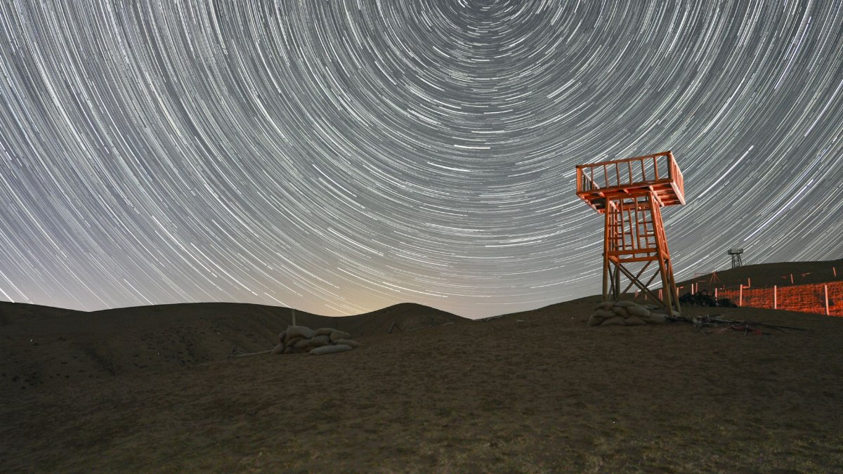 Long exposure photo of star trails over a desert landscape with a wooden observation tower.