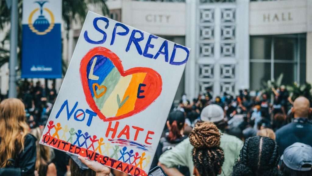 A colorful protest sign promoting love over hate during a rally at City Hall, capturing a peaceful advocacy movement.