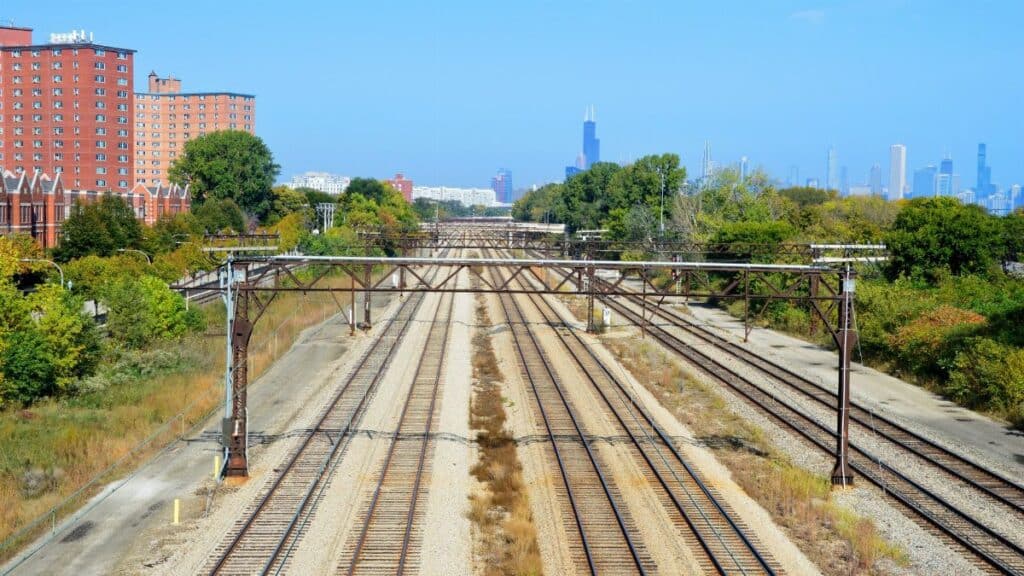 Railroad tracks leading to Chicago skyline with Willis Tower visible, under a clear blue sky.