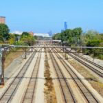 Railroad tracks leading to Chicago skyline with Willis Tower visible, under a clear blue sky.