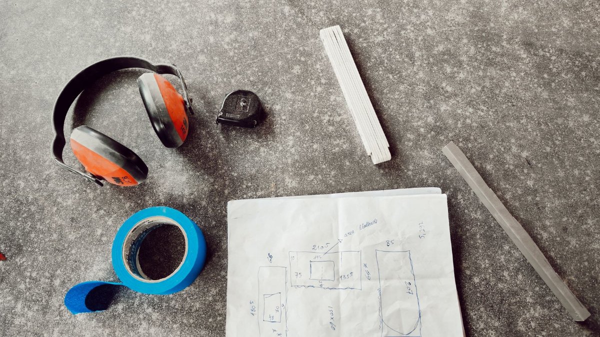 Overhead view of engineering tools including headphones, tape, and a sketch on a workbench.
