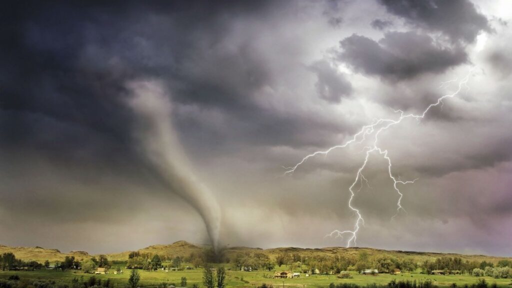 A powerful tornado and vibrant lightning striking over a rural countryside landscape.