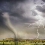 A powerful tornado and vibrant lightning striking over a rural countryside landscape.