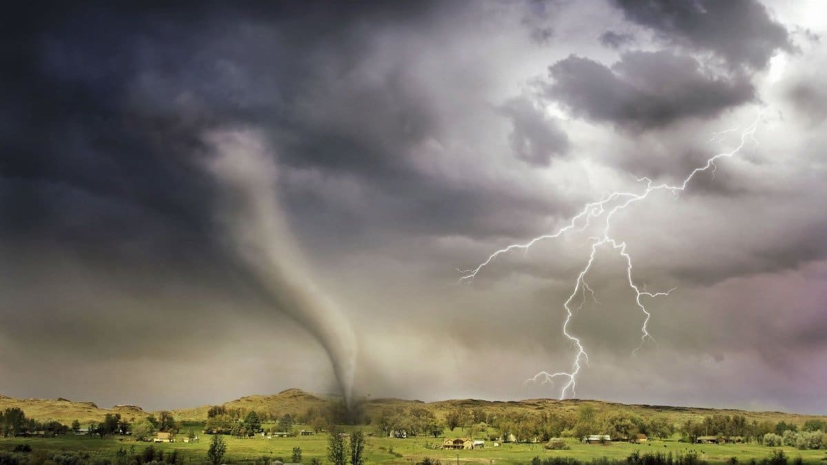 A powerful tornado and vibrant lightning striking over a rural countryside landscape.