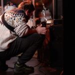 A musician wearing a patterned sweater tunes an amplifier on stage before a live performance.