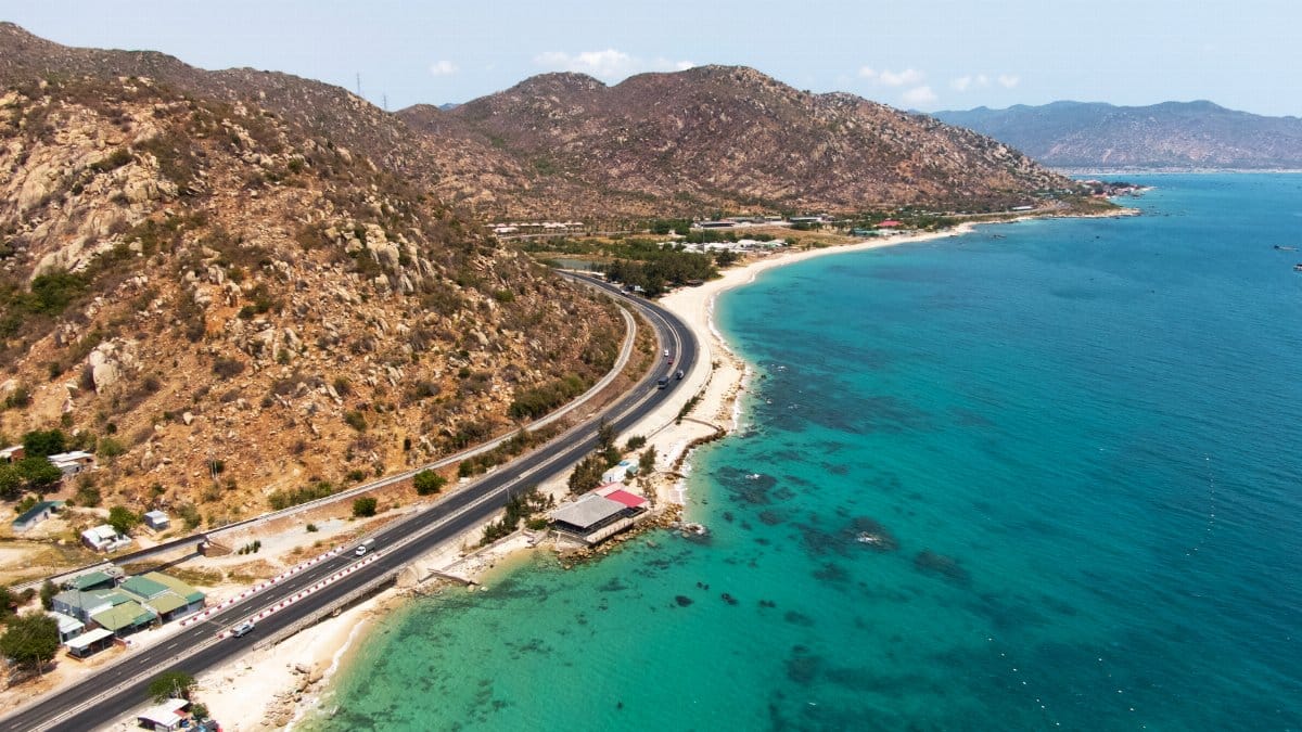 Aerial view of scenic coastal road alongside a vibrant blue sea and rocky mountains.