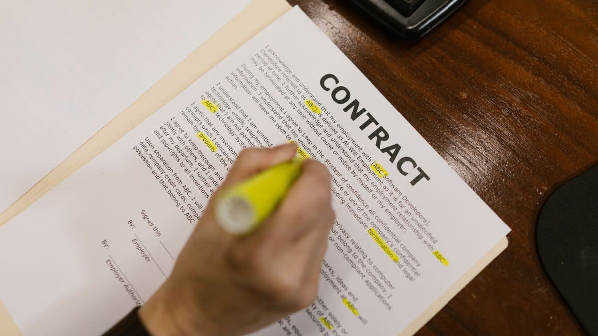 Focused view of a person highlighting text in a contract document on a wooden office desk.
