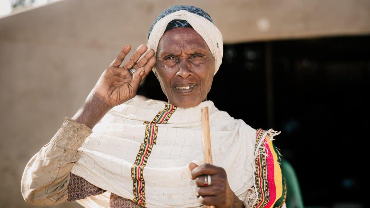 Portrait of an elderly Ethiopian woman in traditional clothing, posing with a gesture outdoors.
