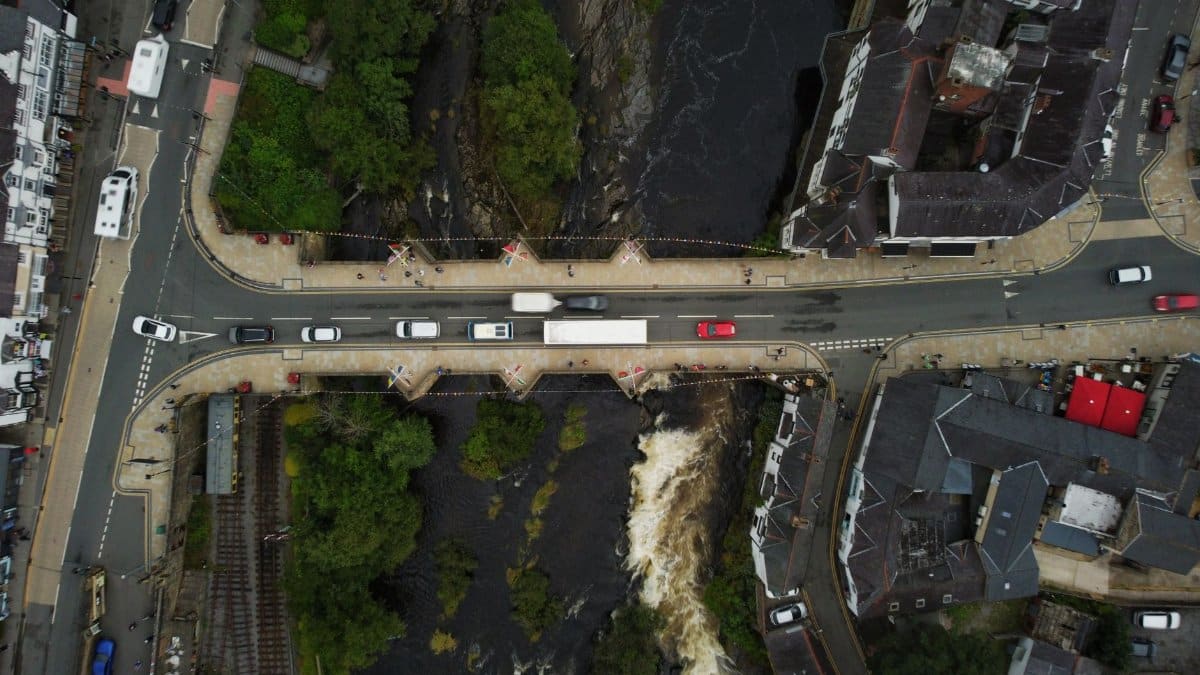 Aerial shot capturing traffic over a bridge surrounded by urban buildings and a flowing river.