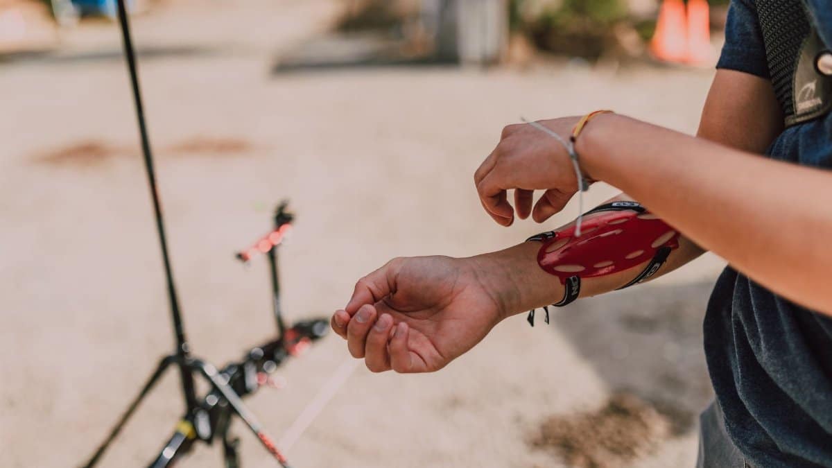 Close-up of a person adjusting an archery arm guard outdoors, showcasing archery preparation.