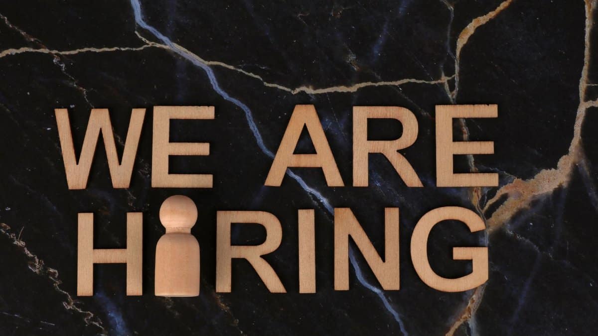 Wooden letters spell 'We Are Hiring' on dark marble surface.