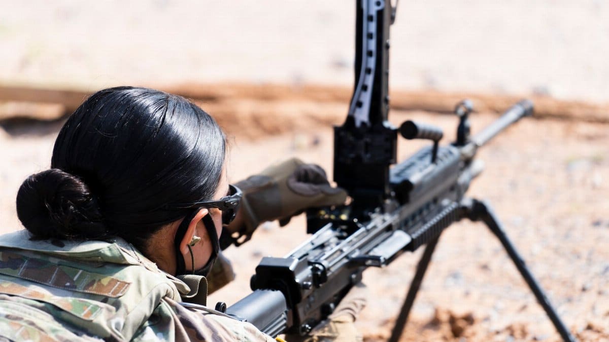 A female soldier in military uniform operates a machine gun during combat training outdoors.