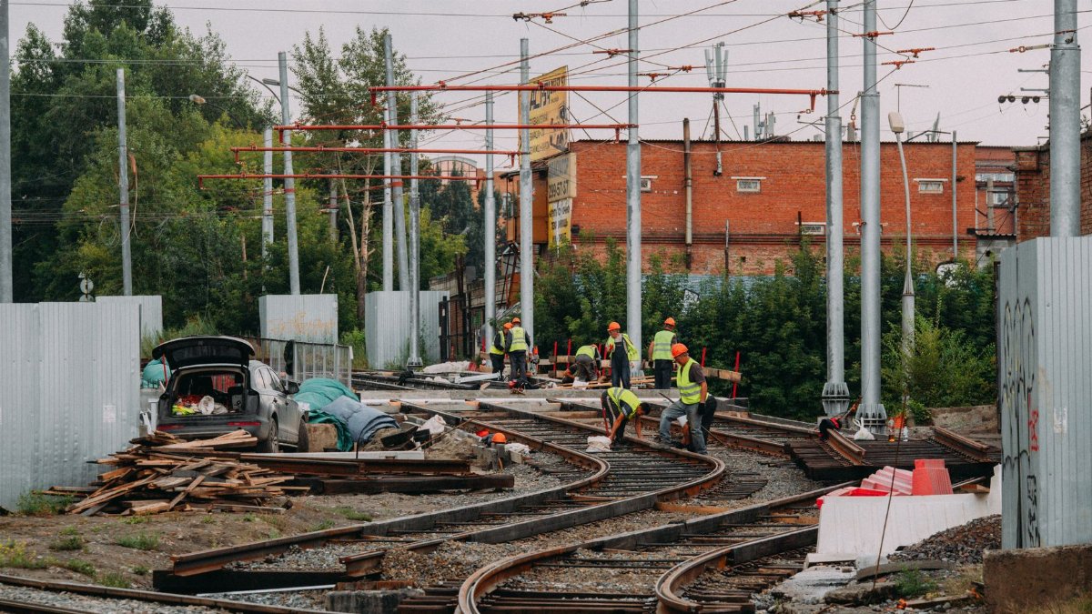 Workers repairing train tracks outdoors amidst an urban setting, emphasizing industry and teamwork.