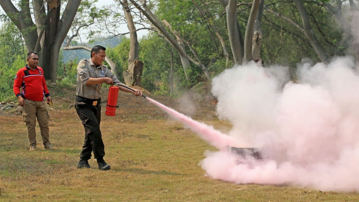 A fire safety officer demonstrates use of an extinguisher during outdoor training, releasing pink smoke.