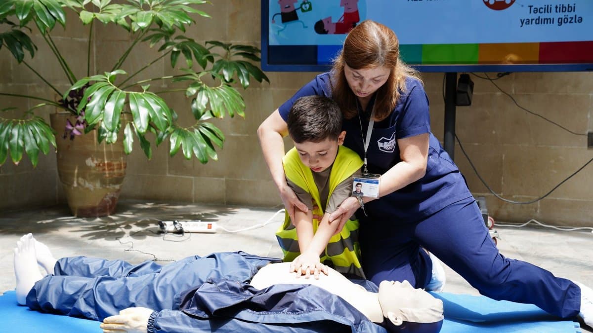 Nurse guides child in CPR training using a dummy indoors.