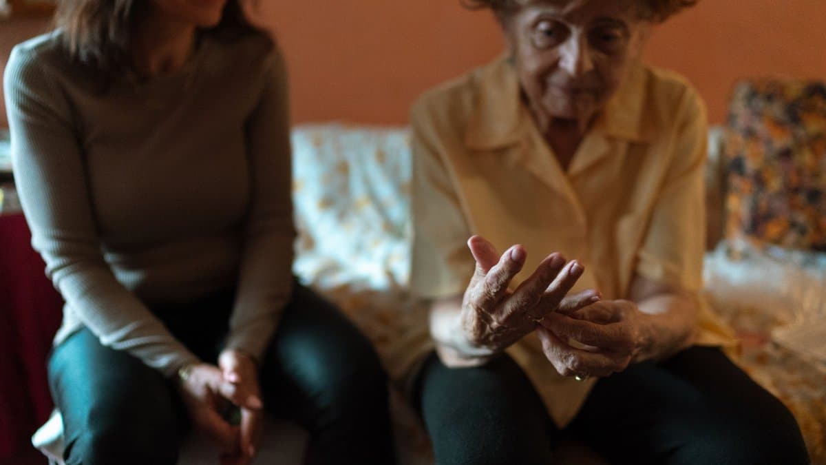 An elderly woman and her caregiver share a moment on the couch, embodying companionship.