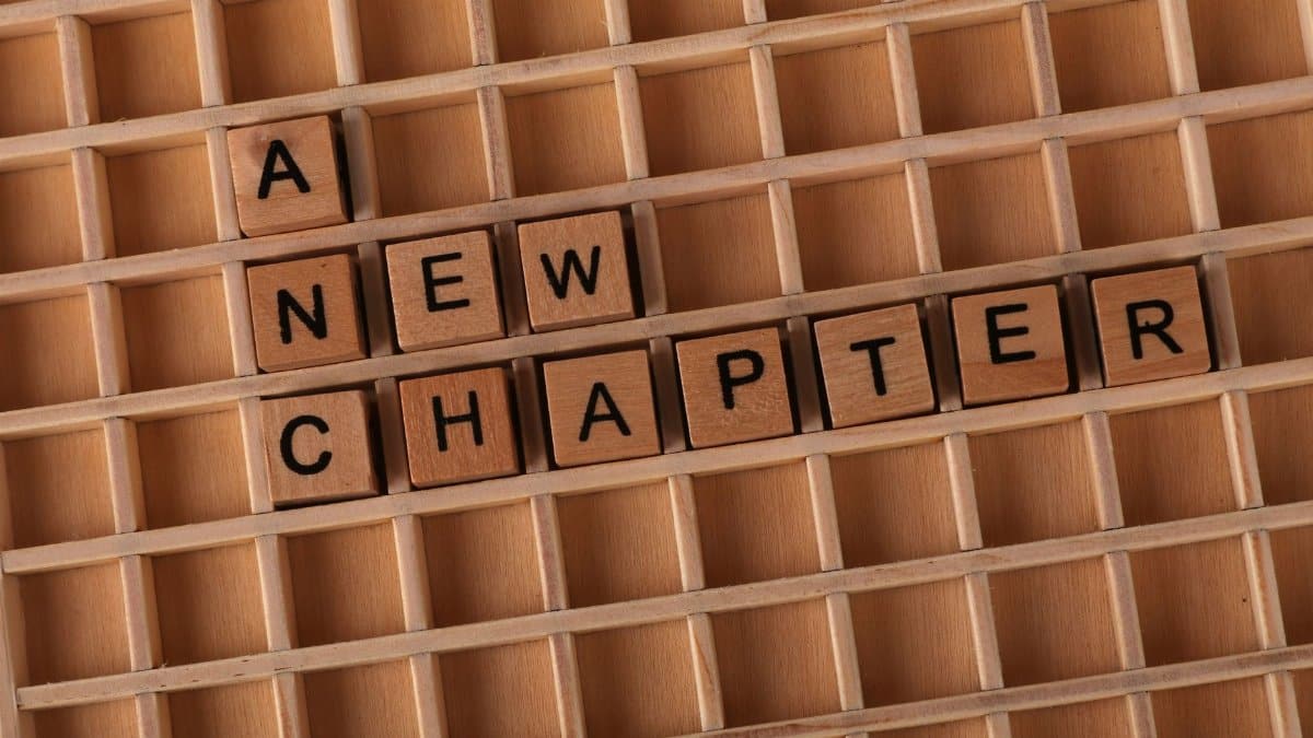 Wooden Scrabble letters arranged to spell 'A New Chapter' on a gridded board.
