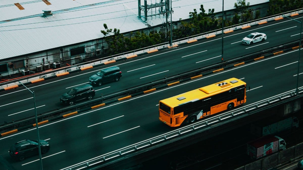 From above of modern yellow bus and various cars driving on asphalt road in city