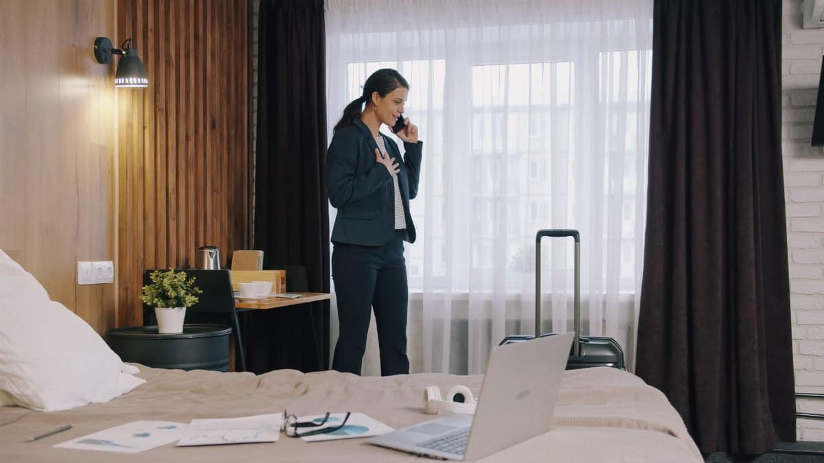 Businesswoman in hotel room talking on phone, representing work travel.
