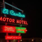 Colorful neon lights illuminate a vintage motel sign at night along the roadside.