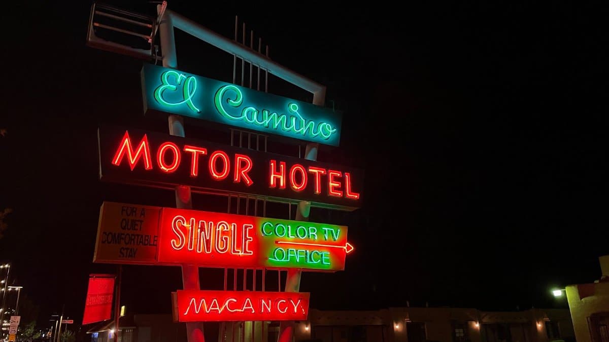 Colorful neon lights illuminate a vintage motel sign at night along the roadside.