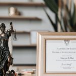 A framed Harvard Law School certificate beside a Lady Justice statue on an office desk.