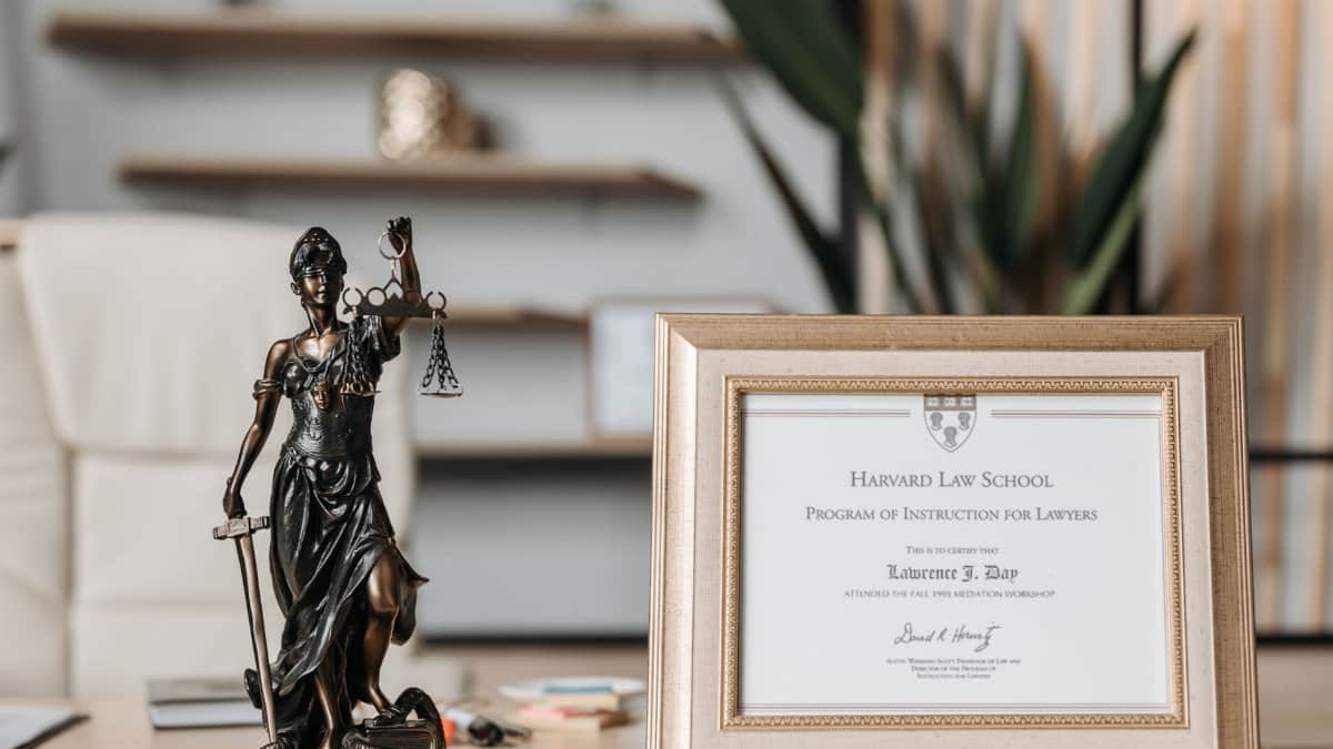 A framed Harvard Law School certificate beside a Lady Justice statue on an office desk.