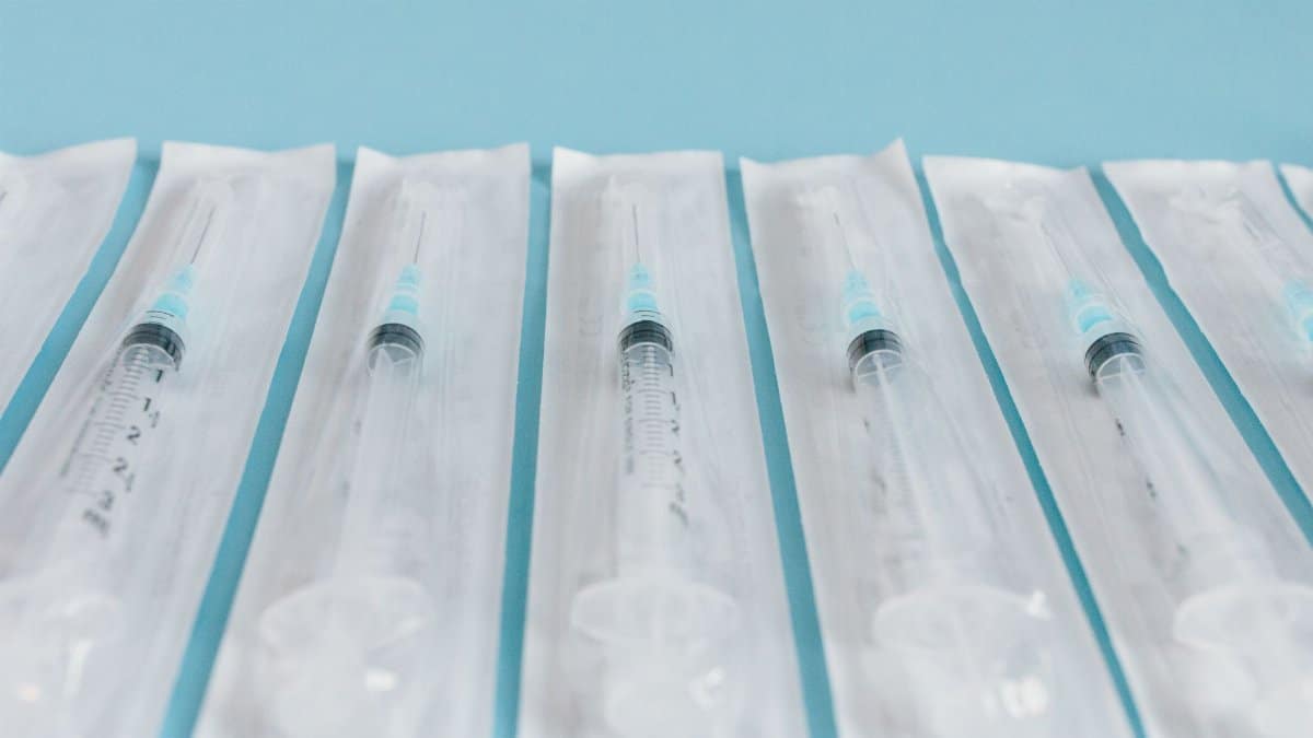 Array of sterile syringes in individual packaging against a blue background.