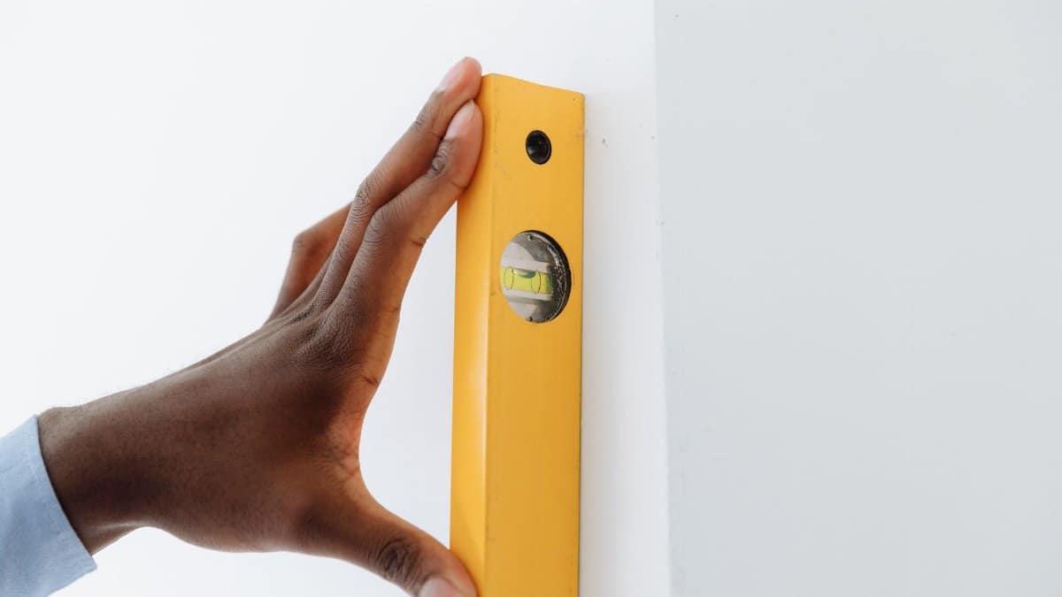 A close-up of a hand using a yellow level tool against a white wall to ensure vertical alignment.