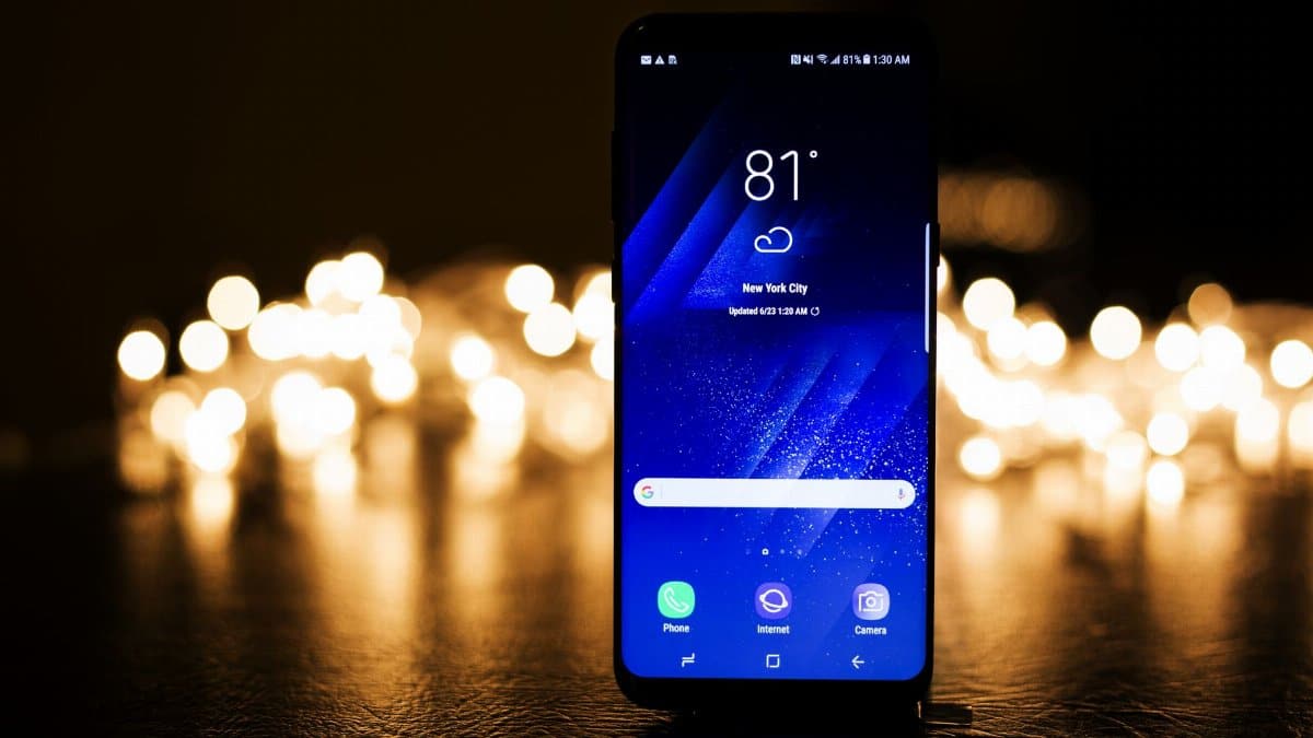 Illuminated smartphone screen showing New York City weather forecast at night.