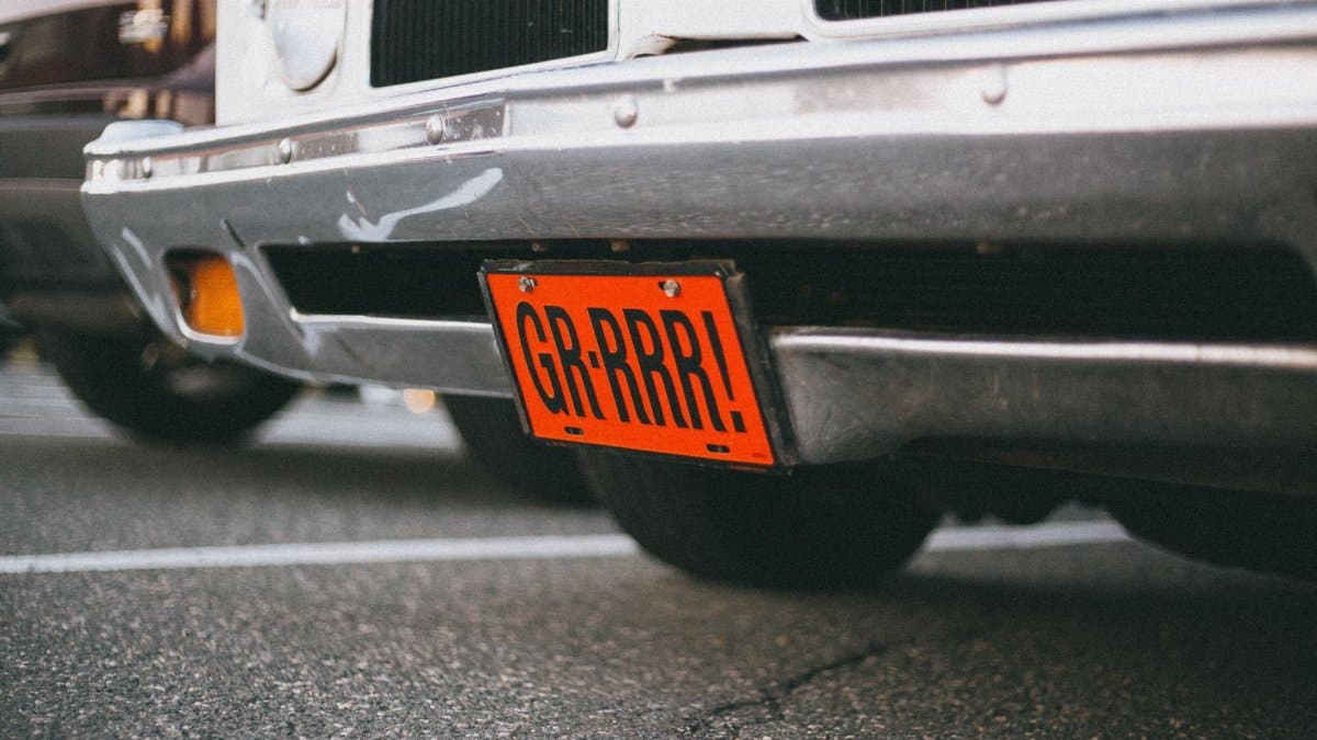 Close-up of a vintage car with a custom orange license plate reading 'GR-RRR!' in a parking lot.