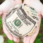 Hands holding crumpled money outdoors, symbolizing charity and financial support.