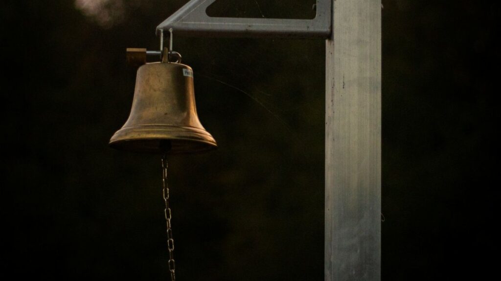 A close-up of a brass bell on a post with a chain at dusk, creating a moody ambiance.