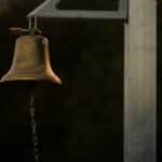 A close-up of a brass bell on a post with a chain at dusk, creating a moody ambiance.