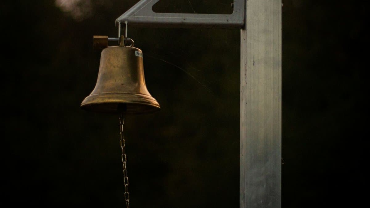 A close-up of a brass bell on a post with a chain at dusk, creating a moody ambiance.