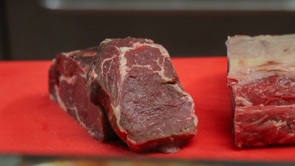 Close-up of raw beef pieces on a red cutting board, showcasing marbling and texture.