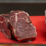 Close-up of raw beef pieces on a red cutting board, showcasing marbling and texture.