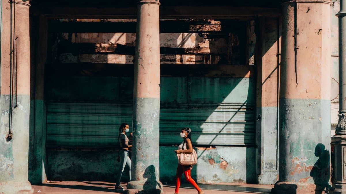 Street photography captures two women walking in La Habana, Cuba, both wearing masks, highlighting urban life.