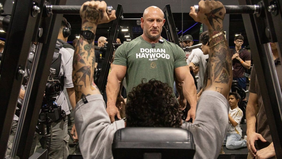 A gym trainer oversees a client's workout on a machine as others observe the session.