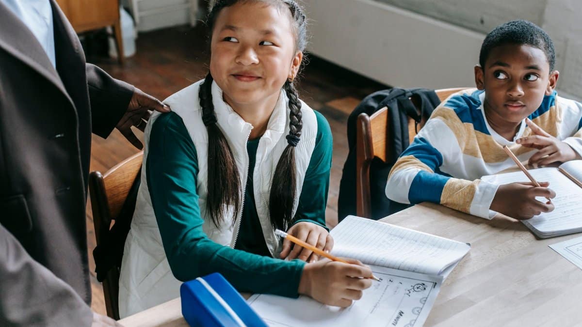 Crop black teacher talking with smart multiethnic boy and girl siting at desk with notepads
