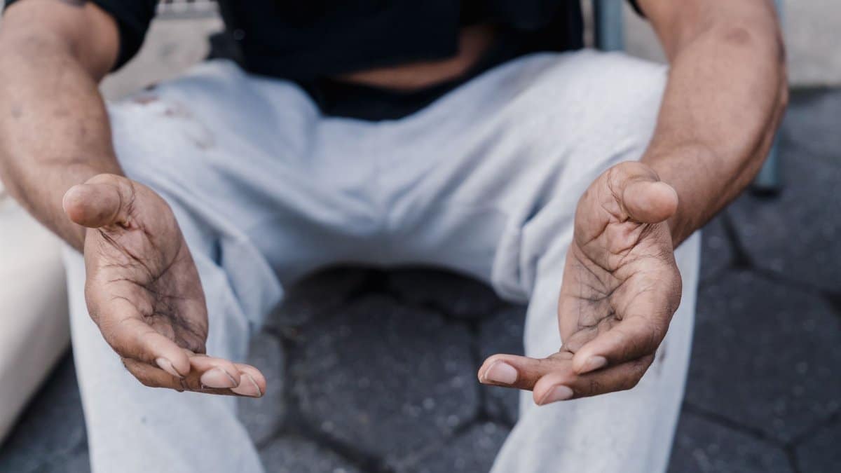 Close-up of outstretched hands of a seated person on a sidewalk, expressing openness.